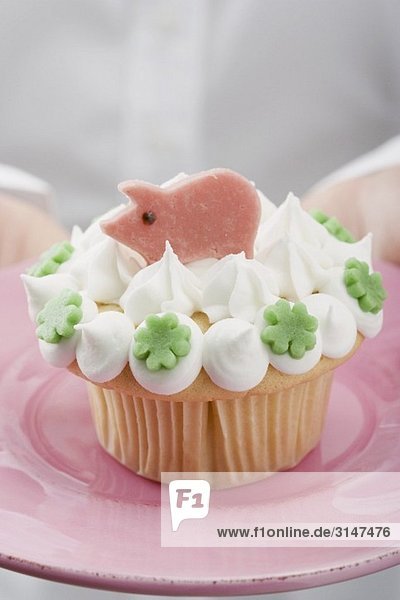 Hände halten Cupcake mit Marzipanschwein auf rosa Teller
