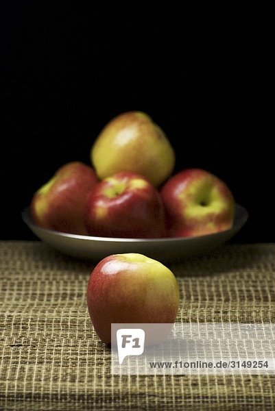 Einzelner Apfel vor einem Teller Äpfel