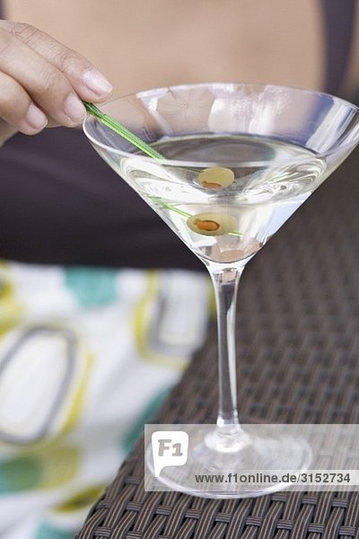 Frau hält Spiesschen mit grüner Olive im Martiniglas