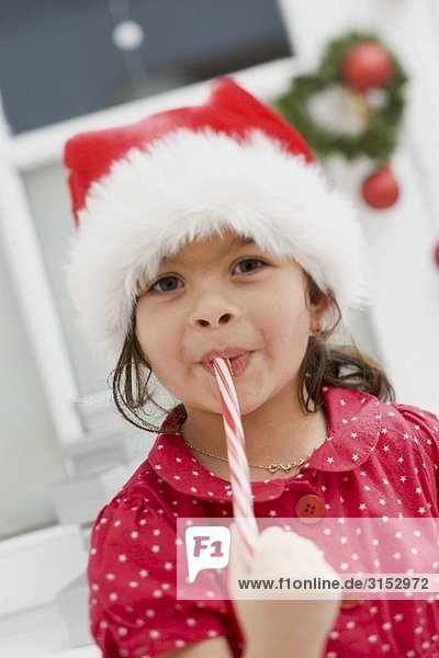 Small girl in Father Christmas hat eating candy cane