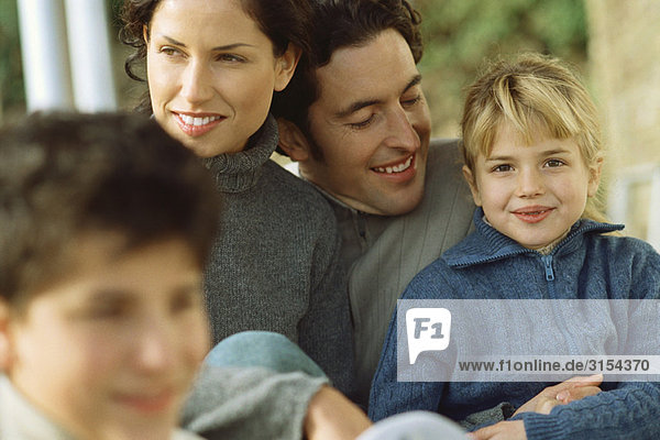 Kleines Mädchen sitzend mit Eltern und Bruder  lächelnd vor der Kamera