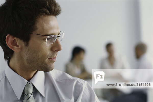 Young businessman in office  turning head to listen to colleagues in background