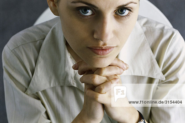Woman with hands clasped under chin  looking at camera  high angle view