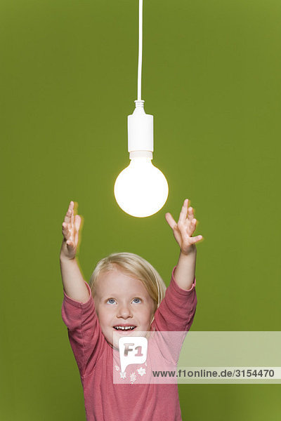 Kleines Mädchen greift nach hängender Glühbirne