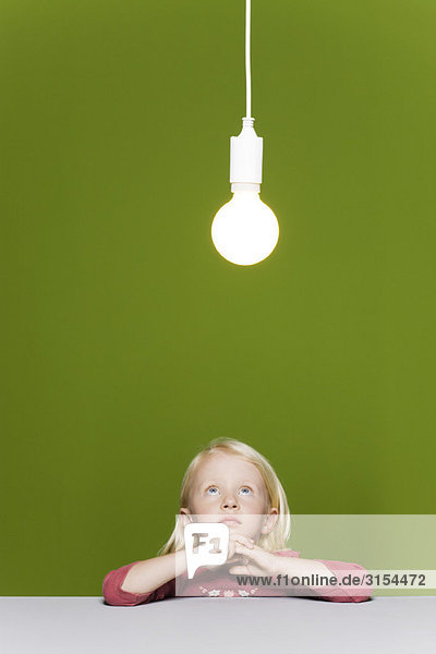 Kleines Mädchen betrachtet beleuchtete Glühbirne oben aufgehängt