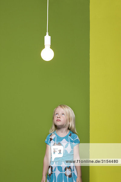 Kleines Mädchen  das auf eine beleuchtete Glühbirne starrt  die über Kopf hängt