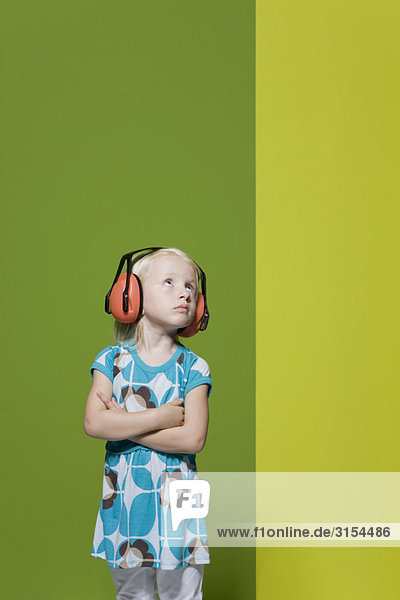 Kleines Mädchen mit gefalteten Armen  mit schützenden Kopfhörern  trotzig wegschauend
