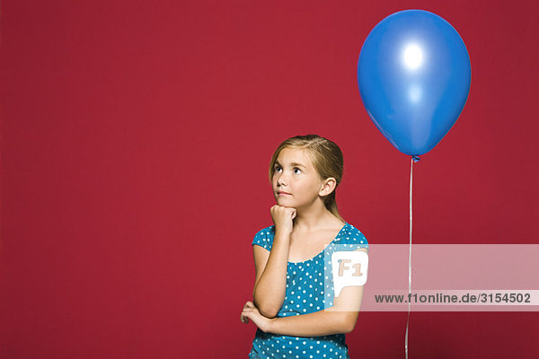 Mädchen mit Hand unter dem Kinn  Ballon hinter ihr aufgehängt