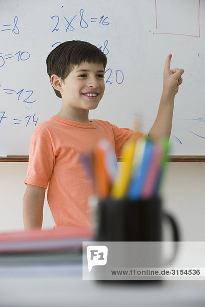 Grundschüler steht vor der Klasse und zeigt auf das Whiteboard.