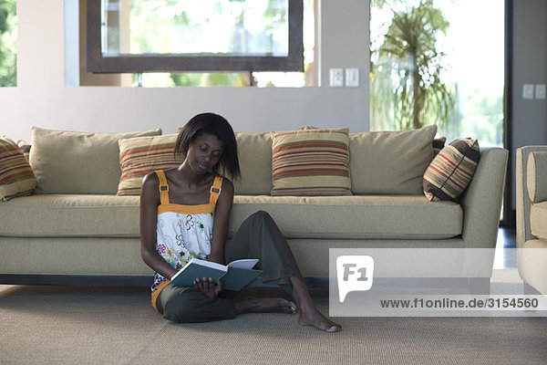 Young woman sitting on living room floor reading book