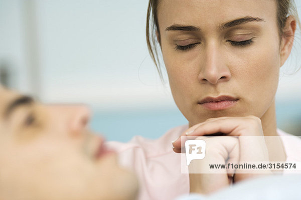 Frau sitzt neben dem schlafenden Mann  die Hände vor dem Gesicht gefesselt  die Augen geschlossen.