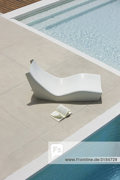 Offenes Buch auf dem Boden neben dem Liegestuhl am Pool liegend  Hochwinkelansicht