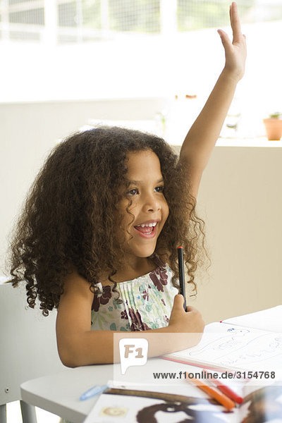 Little girl sitting at school desk  raising hand enthusiastically