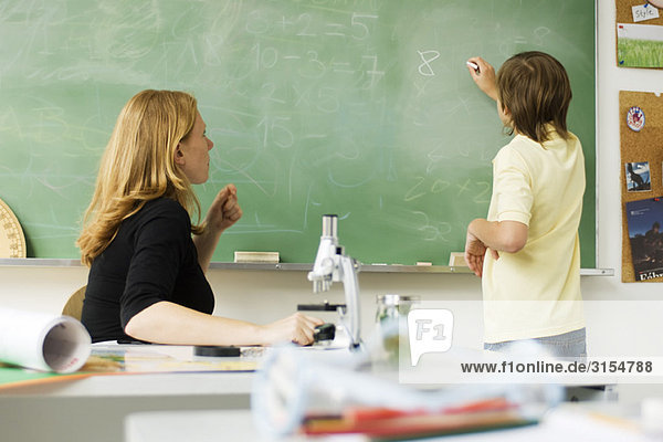 Teacher watching boy writing on blackboard