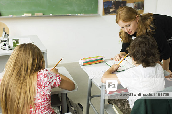 Elementary teacher leaning over student's desk  helping him with assignment