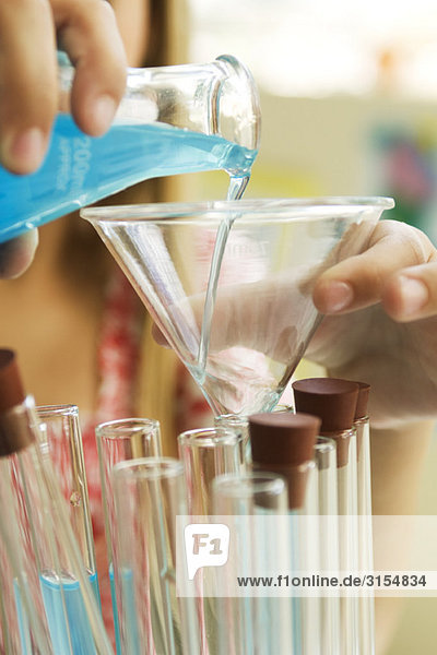 Elementary student transferring liquid from beaker to test tube using funnel  close-up