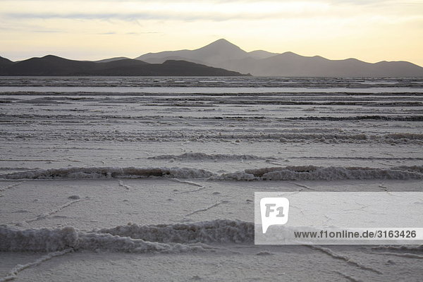 Zu Wellen erstarrtes Salz des Salar de Uyuni mit fernem Gebirge und Abendlicht im Hintergrund