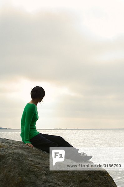 Junge Frau sitzend auf einem Felsen am Meer Schweden.