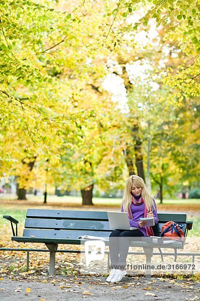 Eine Frau auf Bank in einem Park mit einem Laptop Stockholm Schweden sitzen.
