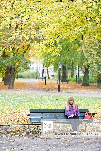 Eine Frau sitzt auf einer Bank in einem Park mit einem Laptop Stockholm Schweden.