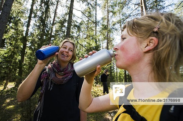 Zwei Frauen Trinkwasser stehen in einem Wald  Sodermanland  Schweden.