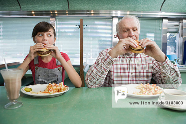 Girl and old man eating burgers in a diner
