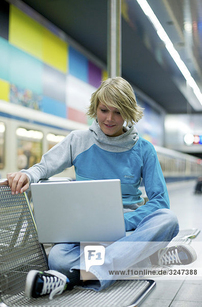 Junge Frau Laptop in S-Bahnstation nutzend  Frontalansicht