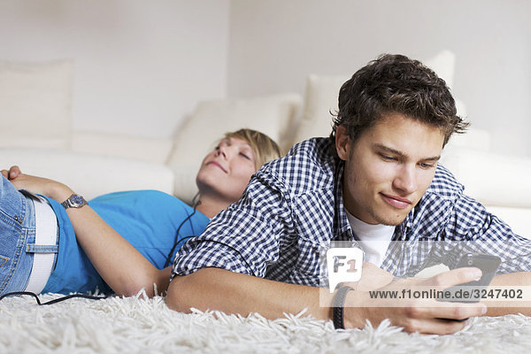 Teenager couple lying on carpet and listening to music  low-angle view