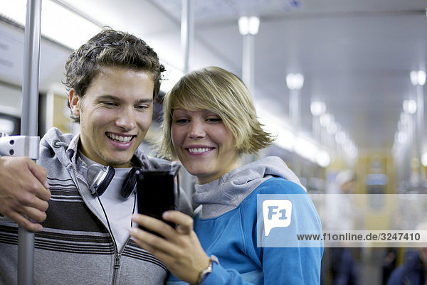 Teenagerpaar in U-Bahn gemeinsam auf Mobiltelefon schauend  Oberkörperaufnahme