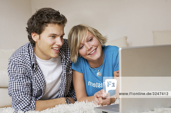 Teenager couple lying on carpet  watching media on notebook  low-angle view