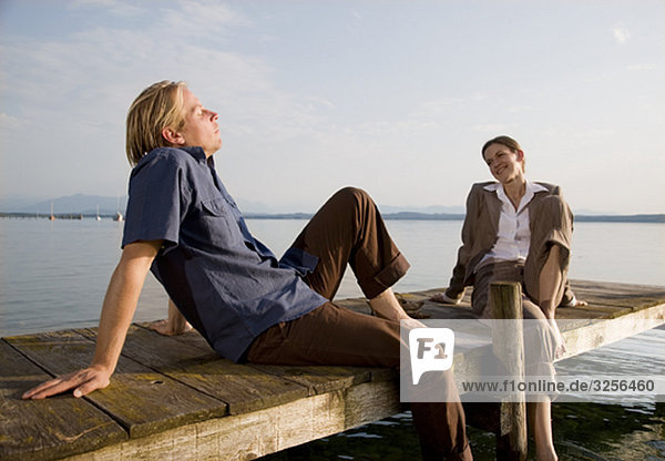Frau und Mann sitzen auf dem Pier am See