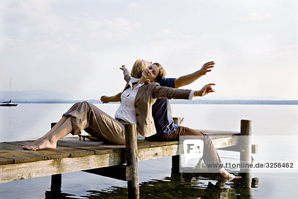 woman and man sitting on pier at lake