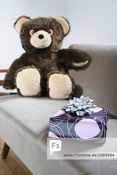Teddy auf Sofa mit Geschenkpaket