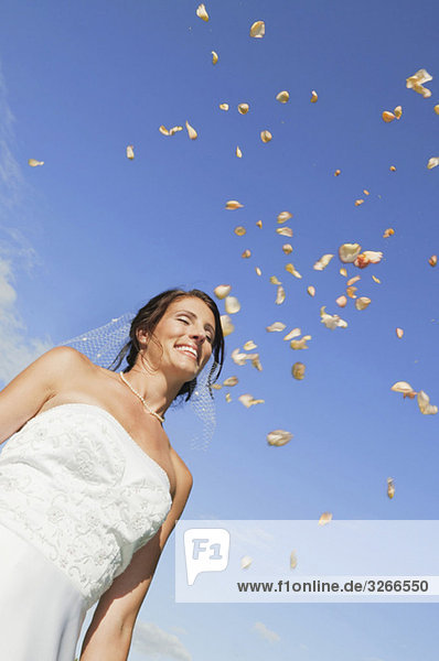 Deutschland  Bayern  Braut lächelnd unter fallenden Blütenblättern  Portrait  Flachwinkelansicht