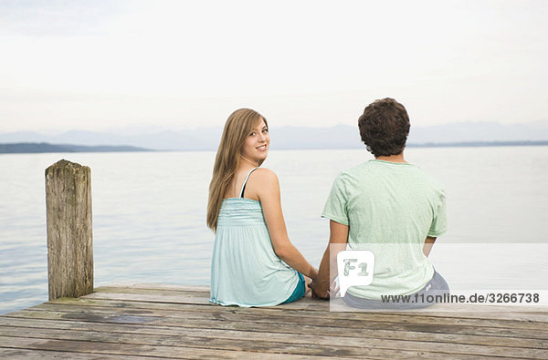 Germany  Bavaria  Starnberger See  Young couple sitting on jetty  rear view