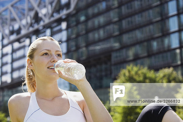 Junge Frau trinkt Wasser aus der Flasche  Gebäude im Hintergrund  Porträt