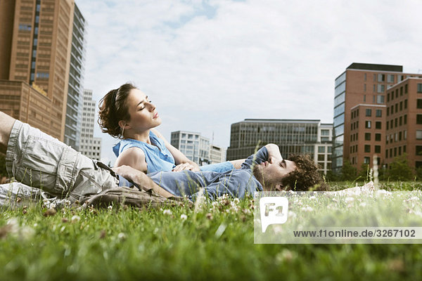 Germany  Berlin  Young couple lying in meadow  high rise buildings in background