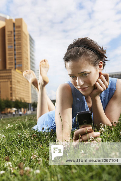 Junge Frau auf der Wiese liegend mit Handy  Porträt