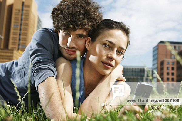 Junges Paar auf der Wiese liegend  Frau mit Handy  Porträt  Nahaufnahme