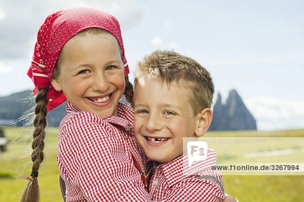 Italien  Seiseralm  Junge (6-7) und Mädchen (8-9) im Feld  umarmend  lächelnd  Portrait  Nahaufnahme