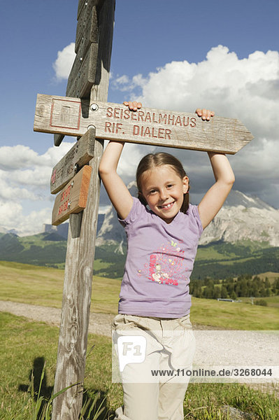 Italy  Seiseralm  Girl (6-7) holding sign post  smiling  portrait