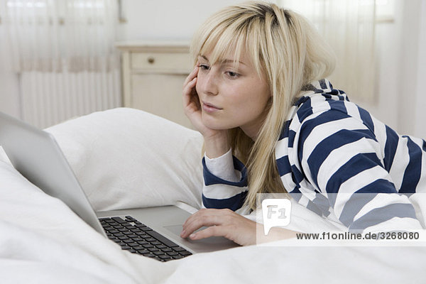 Young woman lying on bed using laptop