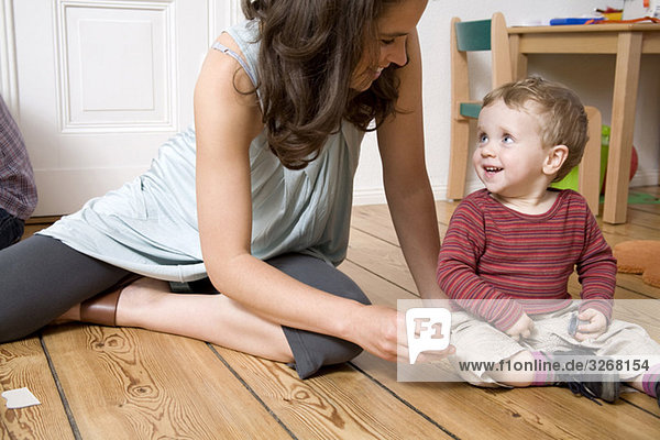 Deutschland  Berlin  Mutter und Sohn (18-23 Monate) auf Holzboden sitzend  lächelnd