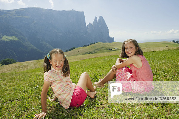 Italy  South Tyrol  Seiseralm Two girls (6-7) (10-11) sitting in meadow