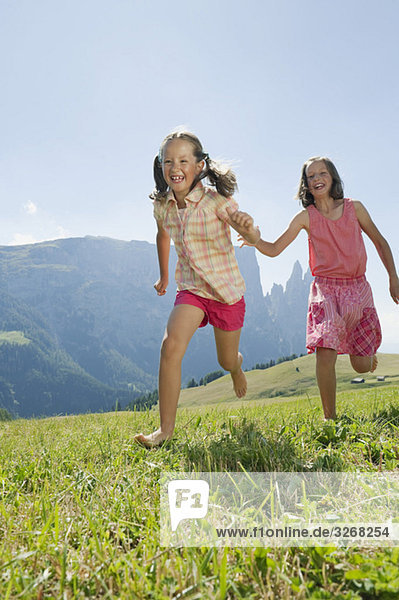 Italy  South Tyrol  Seiseralm  Two girls (6-7) (10-11) running in field