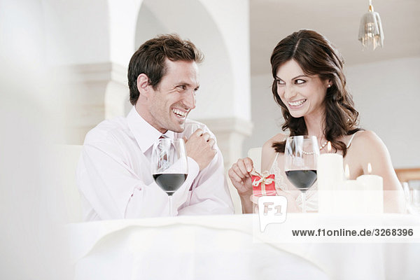 Couple sitting at table in restaurant  woman holding gift parcel