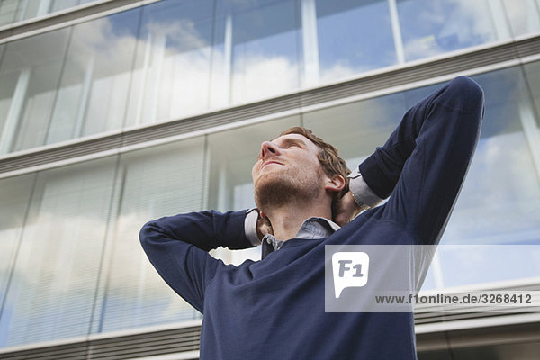 Germany  Hamburg  Businessman in front of office building looking up  low angle view
