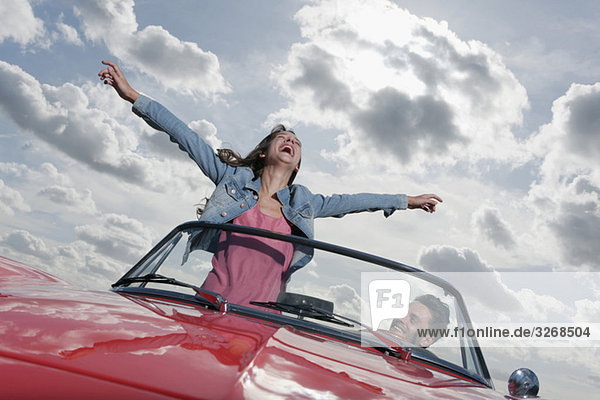 Couple in cabriolet  woman with arms outstretched
