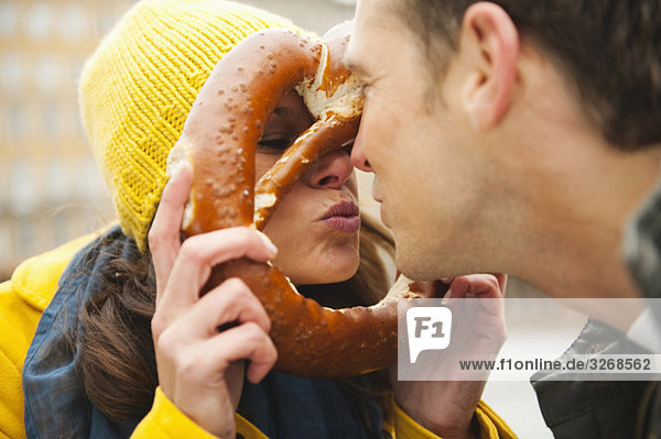 Paar  Frau hält Brezel vor dem Gesicht  Lippen verziehen  Portrait  Mund