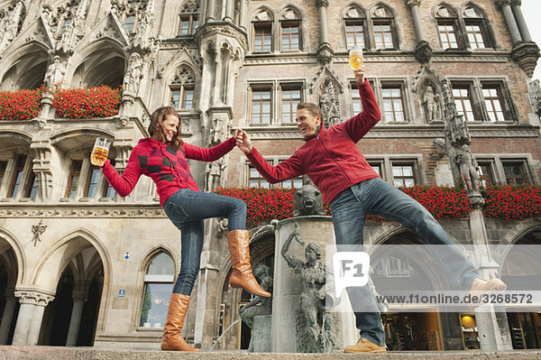 Deutschland  Bayern  München  Marienplatz  Paarbilanzierung am Brunnen  Bierkrüge haltend  lächelnd  Portrait